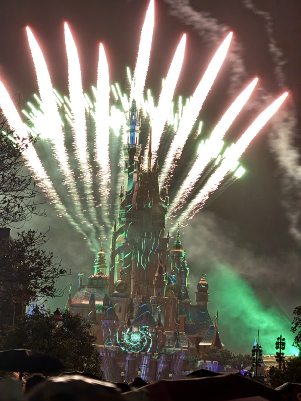 香港ディズニーランドの城に打ち上がる夜の花火。緑と白の光線が城全体を明るく照らしている