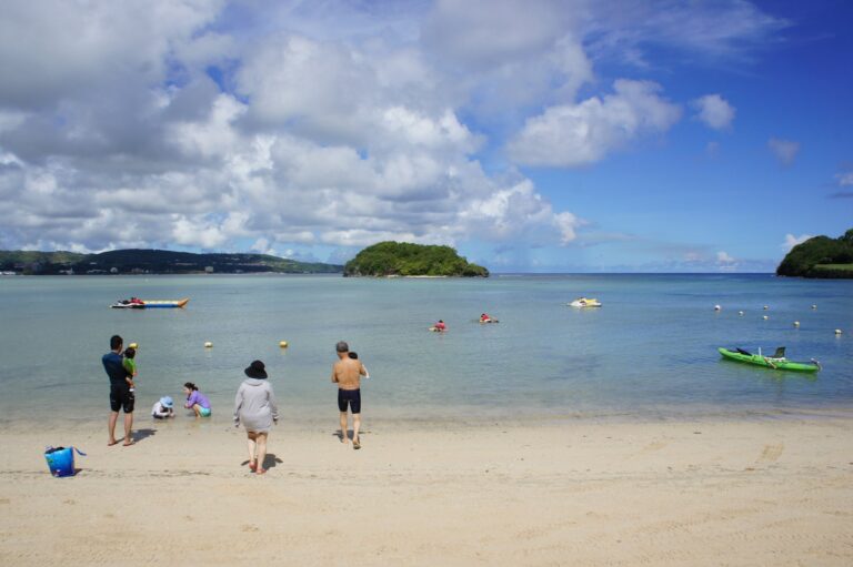 グアムの穏やかなビーチで波打ち際に立つ家族連れ。赤ちゃん連れの三世代グアム旅行