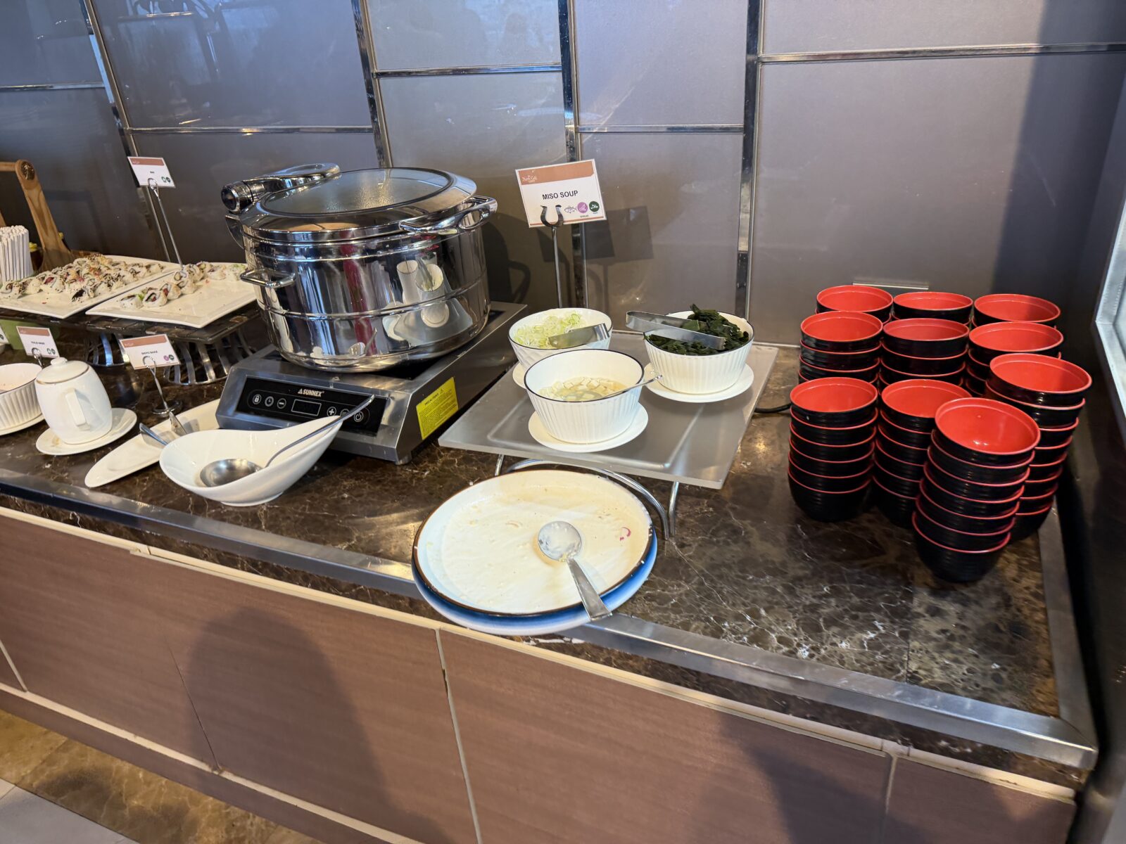 バークレーホテルの朝食にある味噌汁のコーナー。鍋のとなりにねぎとわかめの薬味が置かれ、赤と黒の椀が積まれている
