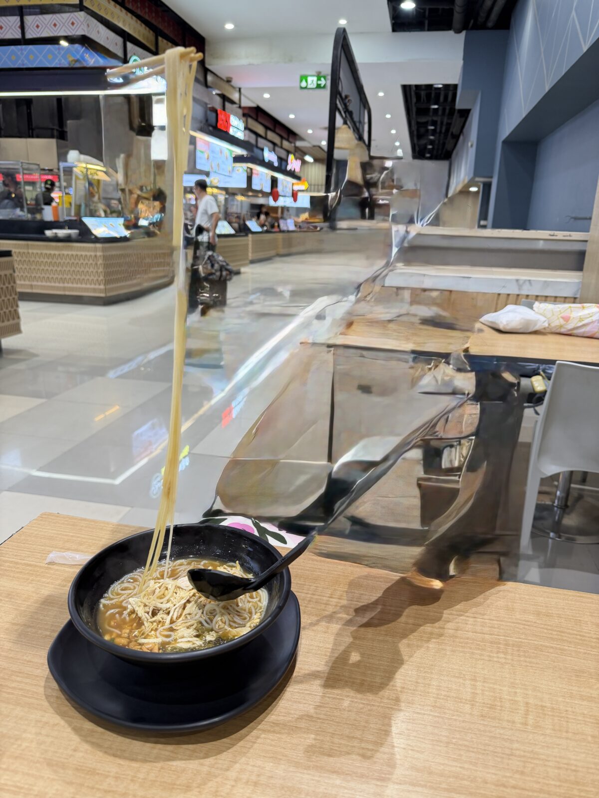 Big Cのフードコートのビーフライスヌードル。黒い器から箸で麺を持ち上げている