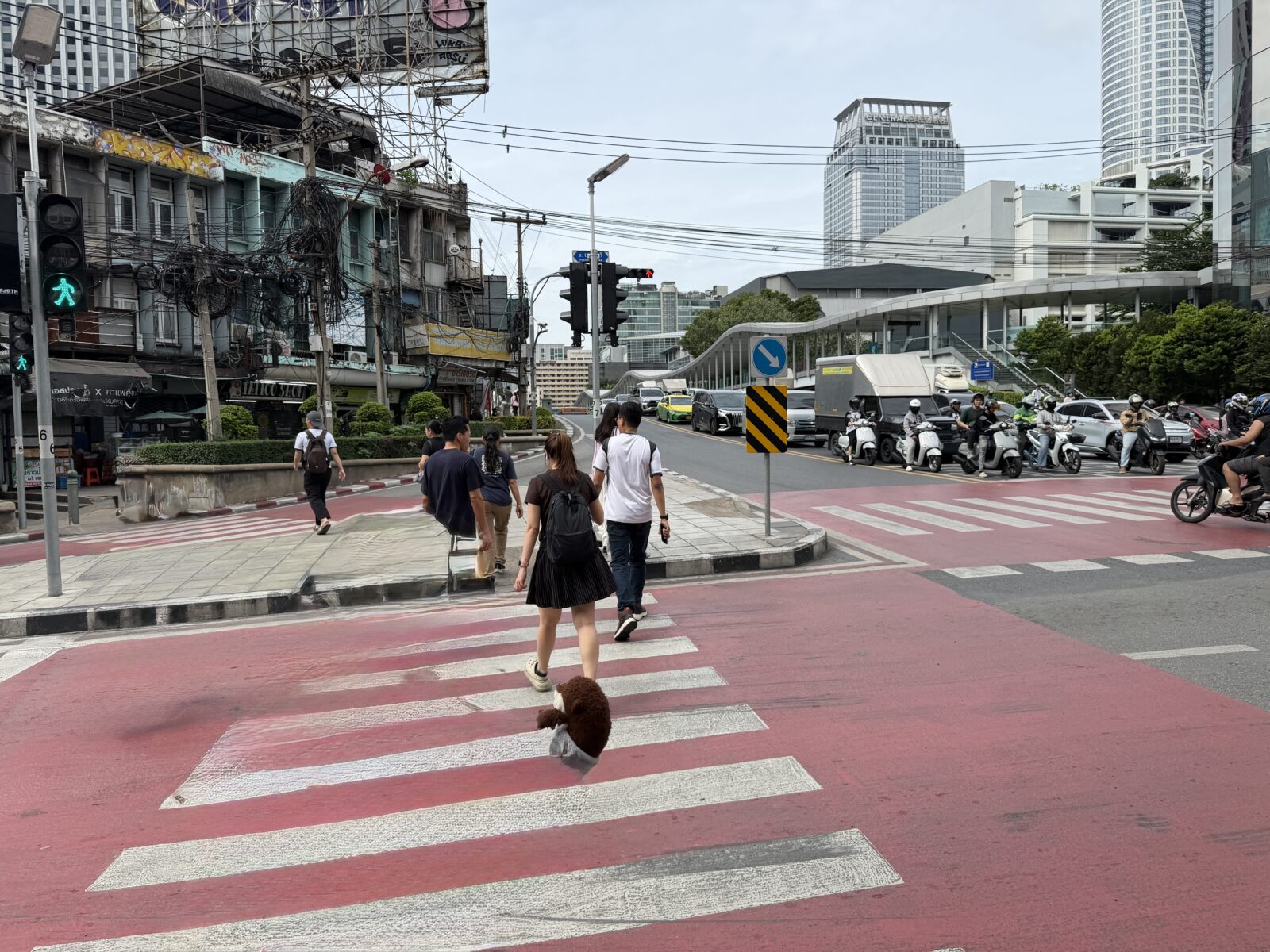 バンコクの大きな交差点の横断歩道。赤く塗られた歩道と行き交う人、バイクが写っている