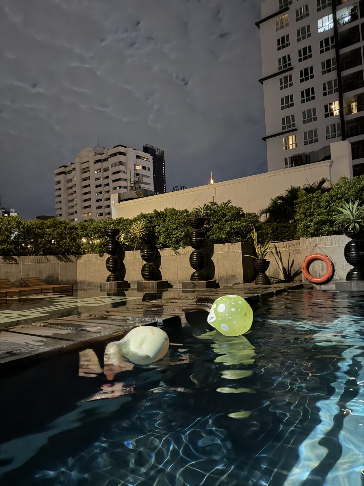 夜のモーベンピックの屋上プールに浮かぶ子ども用の浮き輪とボール。奥に高層マンションの明かりが見える