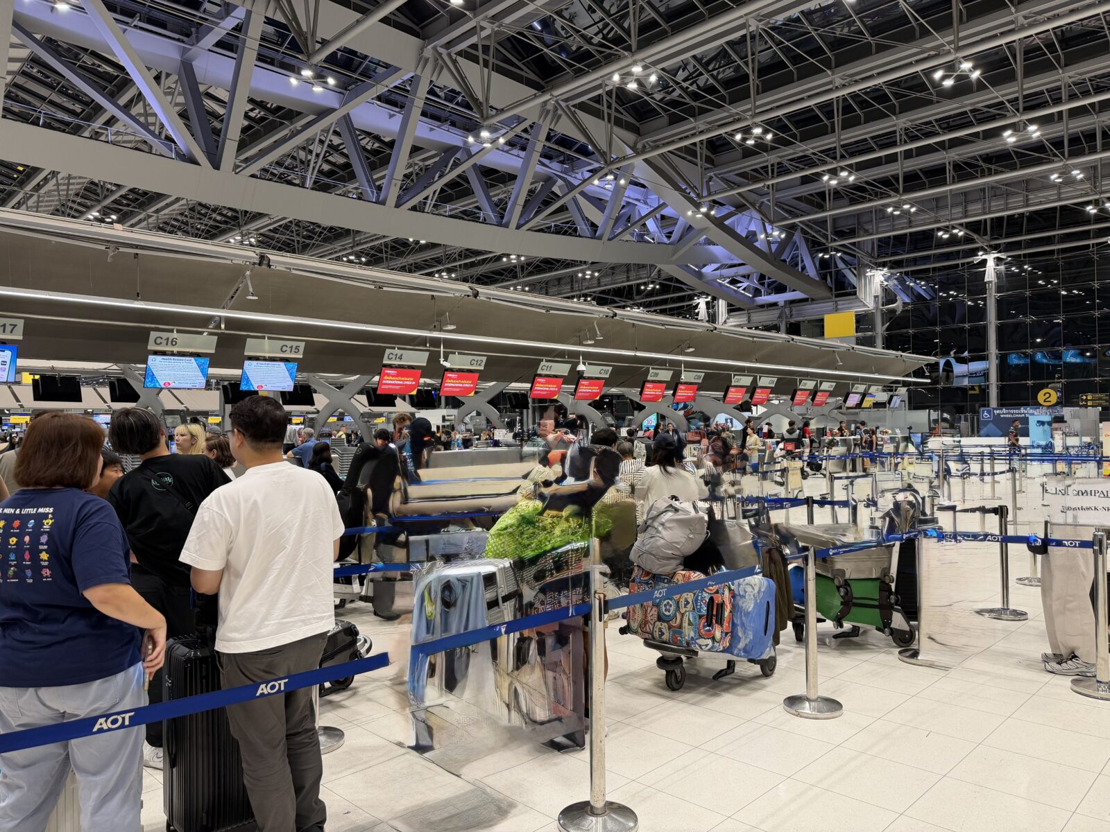 スワンナプーム空港のチェックインカウンター。列に並ぶ乗客とスーツケースが見える