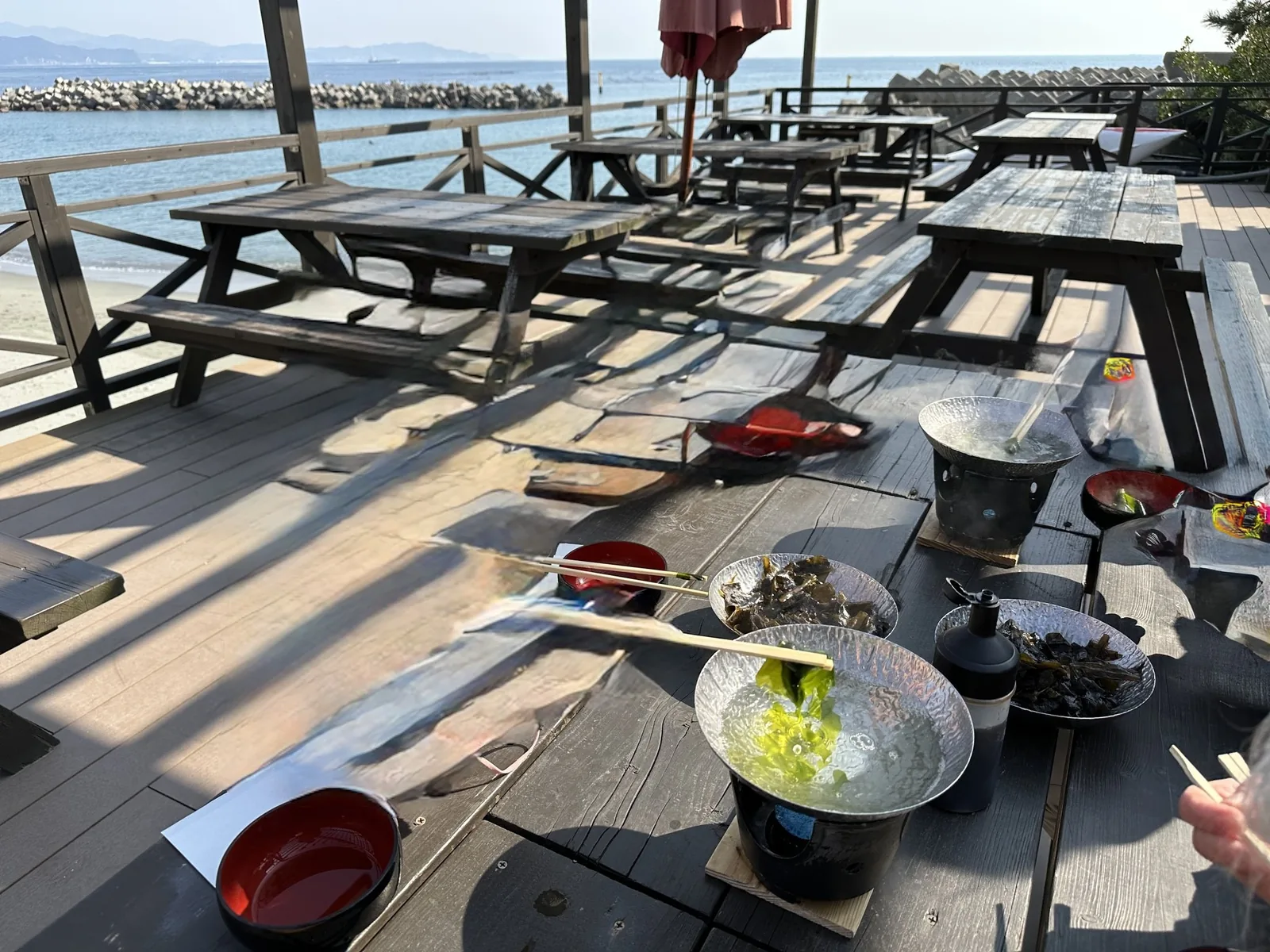 海沿いのテラスの席。鍋に入った緑のわかめと、取り皿やお椀が並ぶ