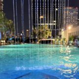ザ・バークレー・ホテル・プラトゥーナムの夜のプール。上から水のカーテンが落ち、照明で青く光る水面の奥にバンコクのビルの夜景が広がる