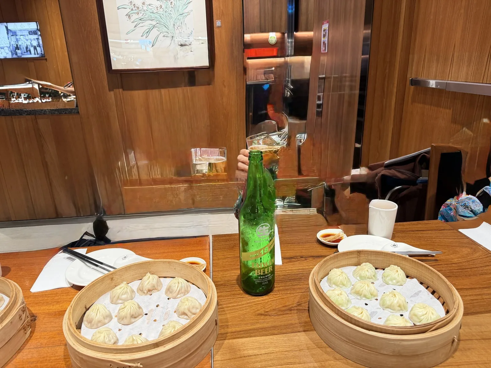 鼎泰豐のテーブルに並んだ小籠包のせいろ2つ。緑瓶の台湾ビールと取り皿が置かれている