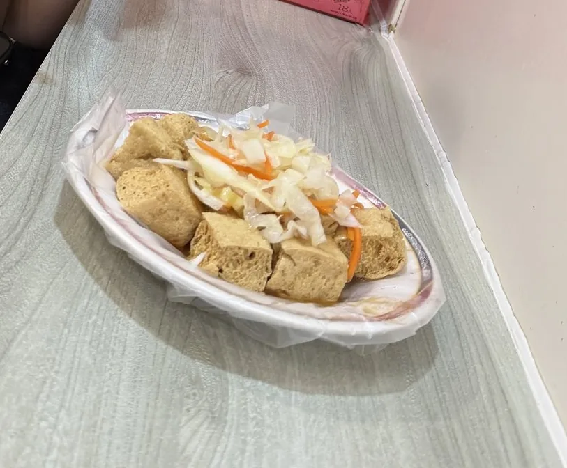 揚げた臭豆腐が4つ、キャベツの漬物を添えて紙の器に盛りつけられている夜市の持ち帰り