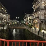 夜の銀山温泉。赤い欄干の橋から、明かりのともった旅館街と川を見たところ