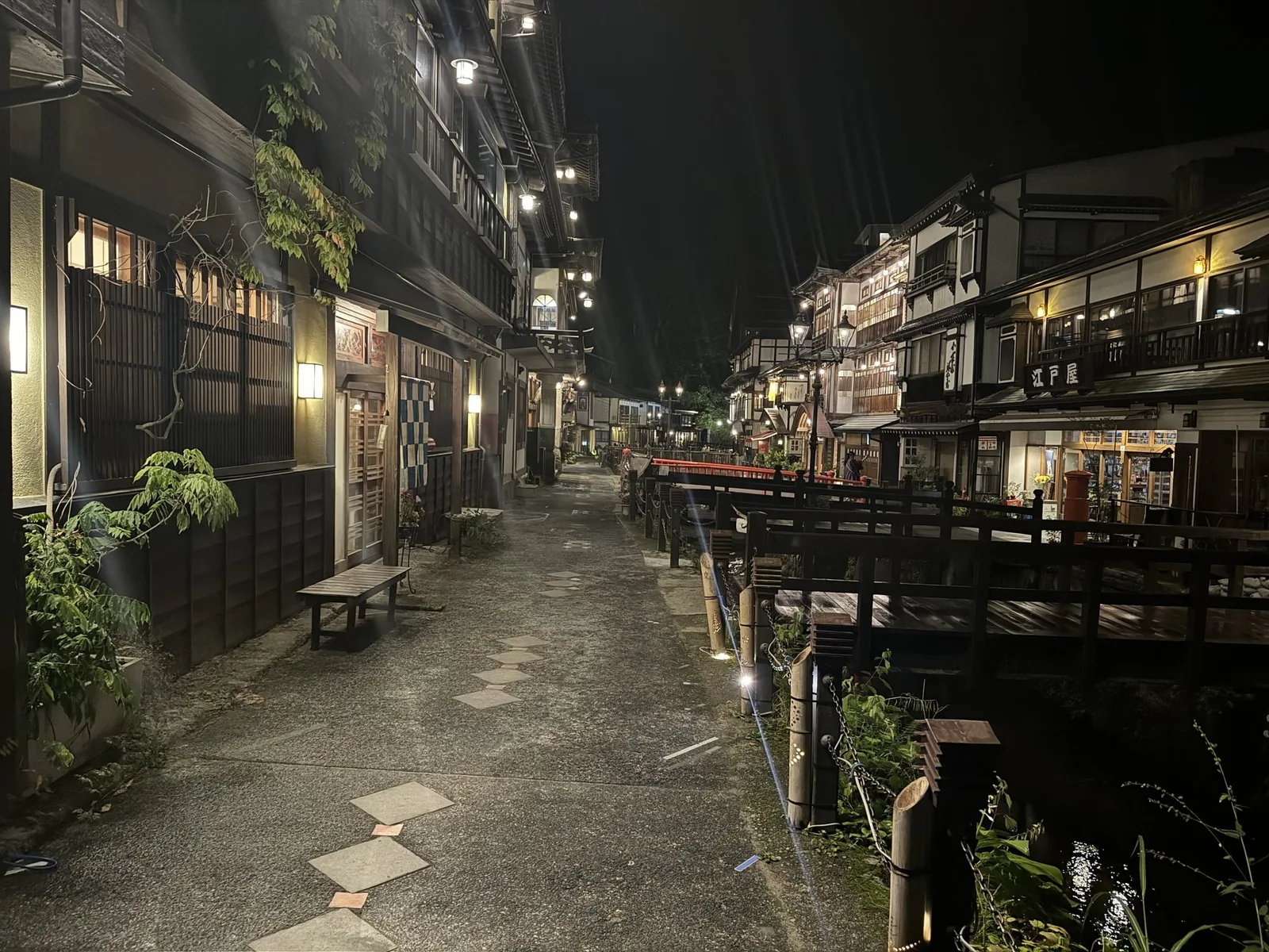 夜の銀山温泉の川沿いの道。石畳と街灯、旅館の明かりが続いている
