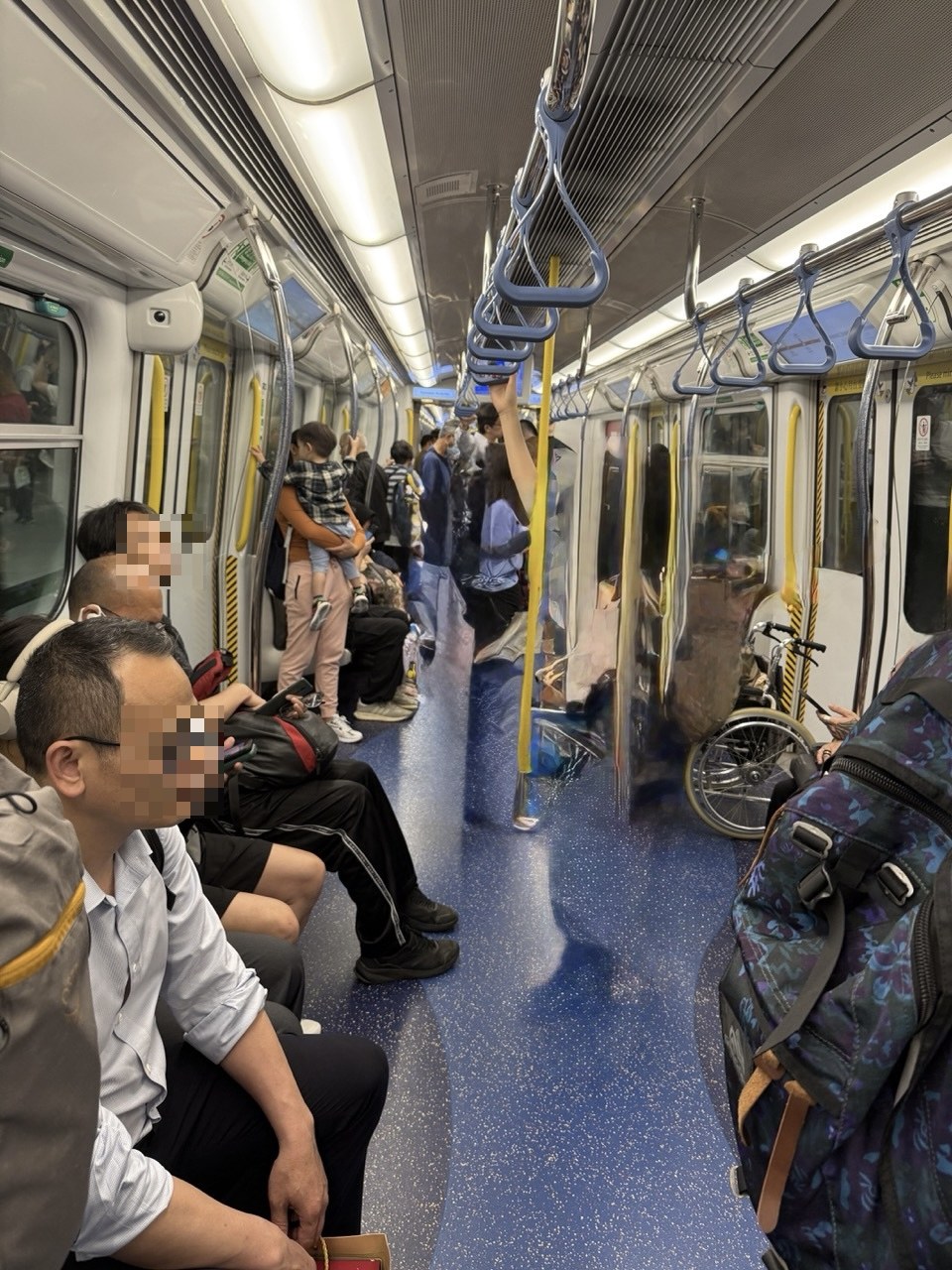 香港のMTRの車内。吊り革と座席が並び、右奥に黄色と黒の斜線で示された車椅子スペースがある