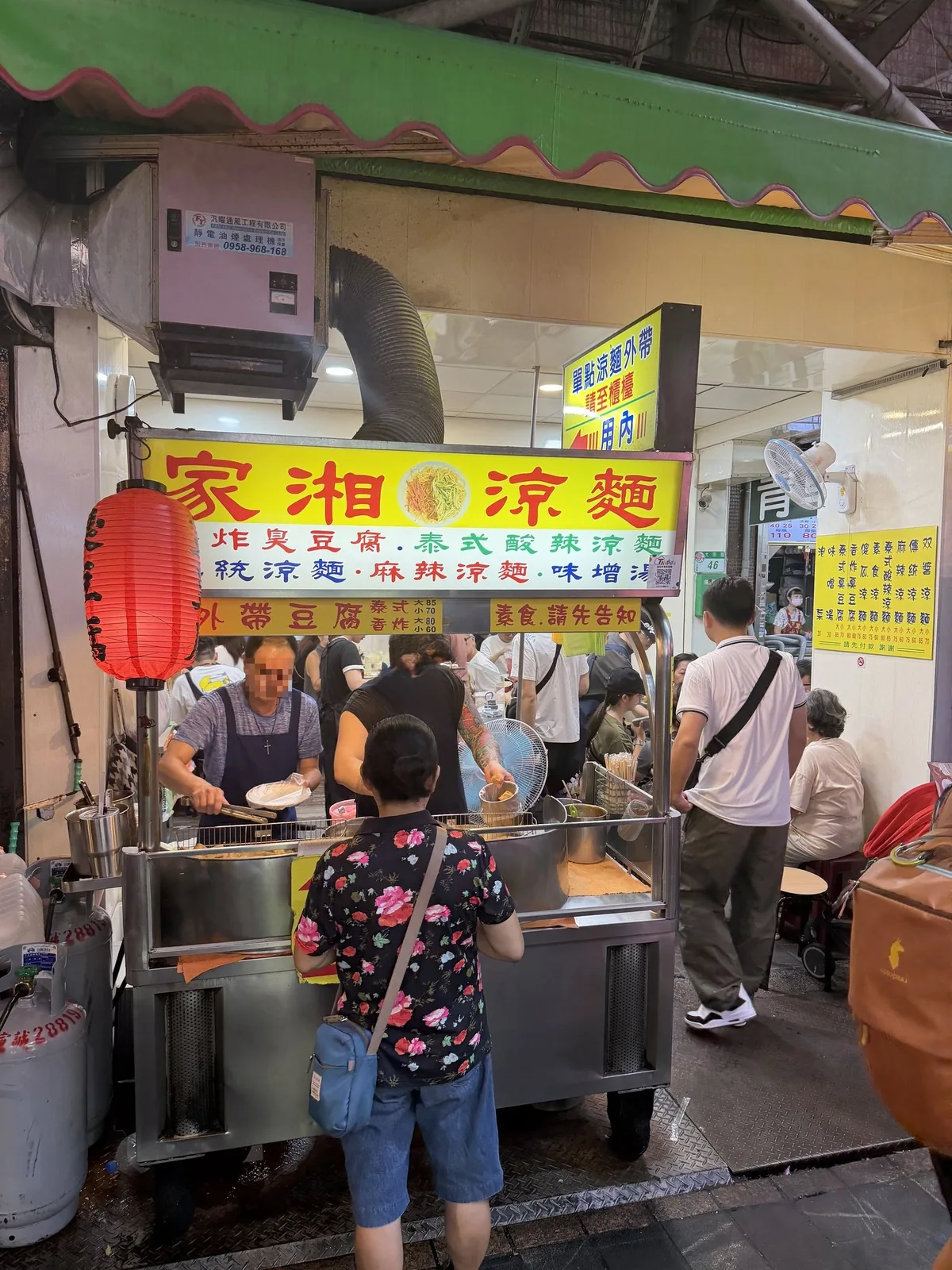 家湘涼麵の店先。黄色い看板の下にある屋台の調理台の前で、客が並んで注文している様子