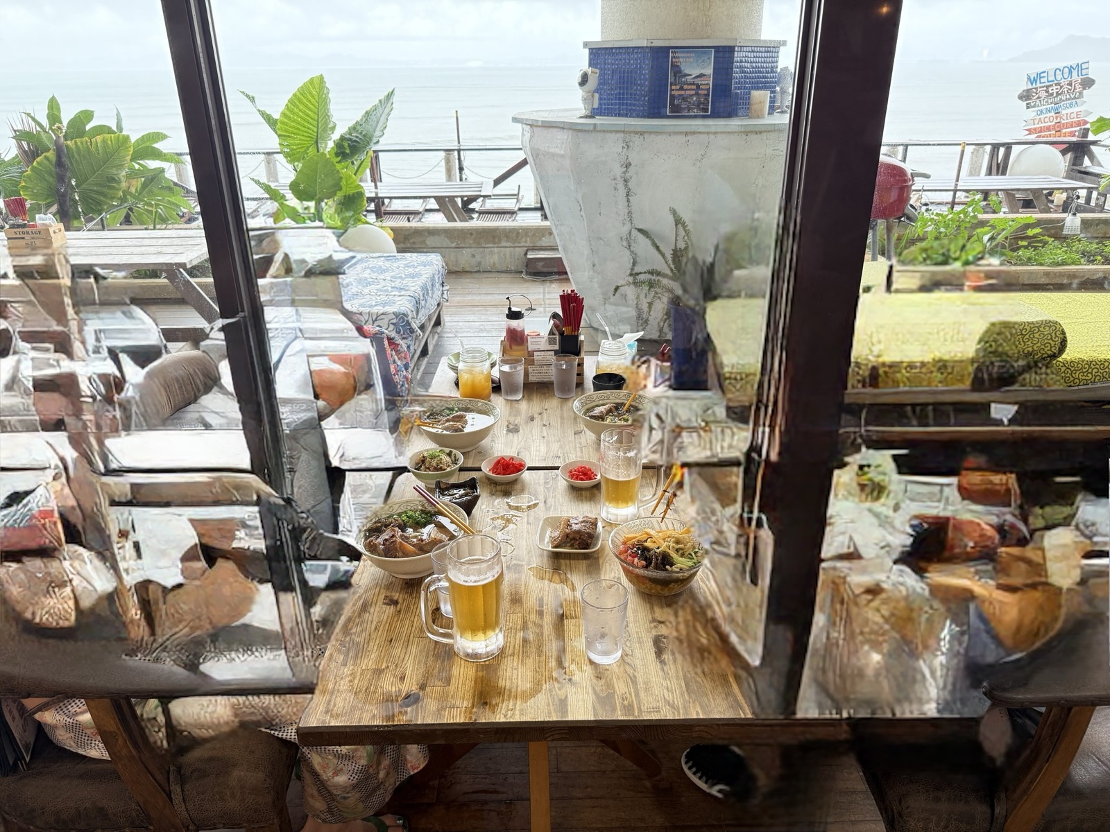 海中茶屋の窓際のテーブル。海を背に生ビールと沖縄料理が並んでいる