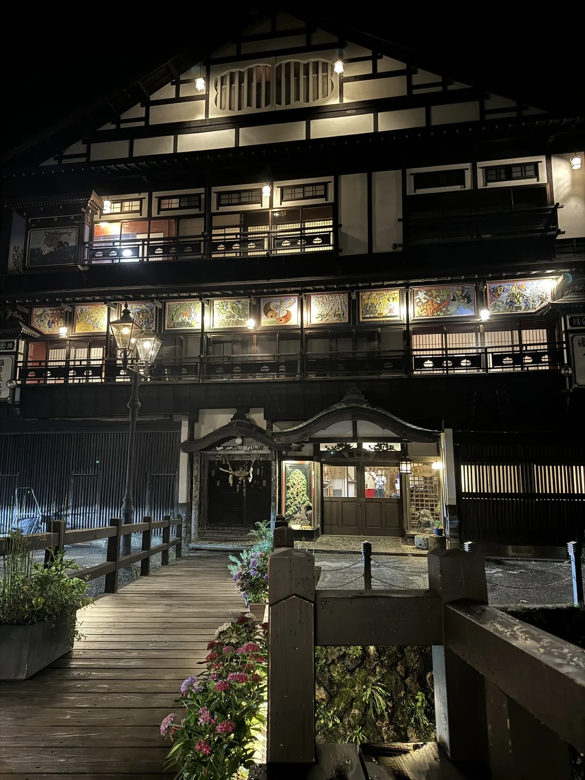夜の古山閣。窓の明かりと絵の飾りがライトアップされた木造の旅館の正面