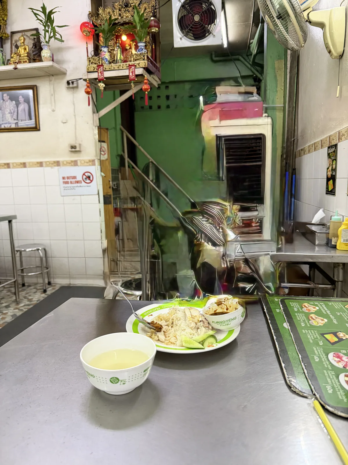 クワンヘンの店内のテーブルに置かれたカオマンガイの皿と、緑の器に入ったスープ