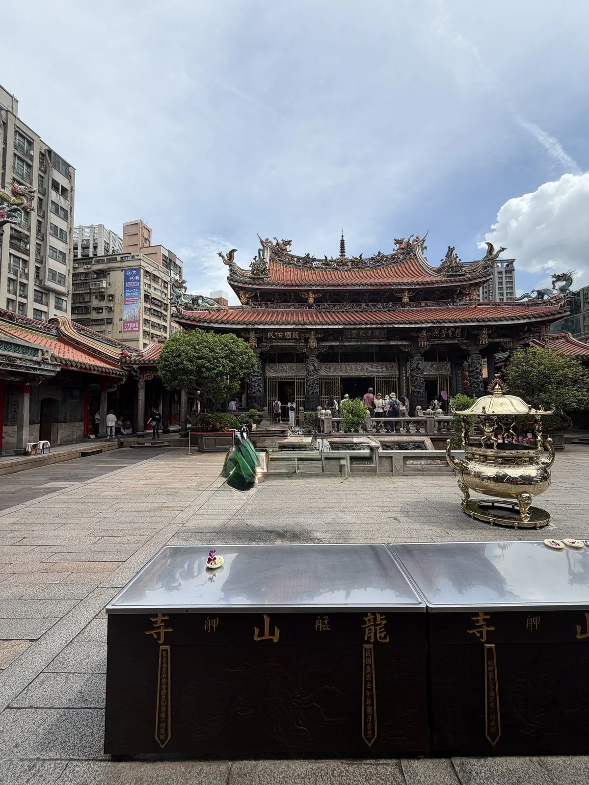 龍山寺の境内。装飾された本堂と大きな香炉が並び、参拝者が歩いている昼どきの静かな様子