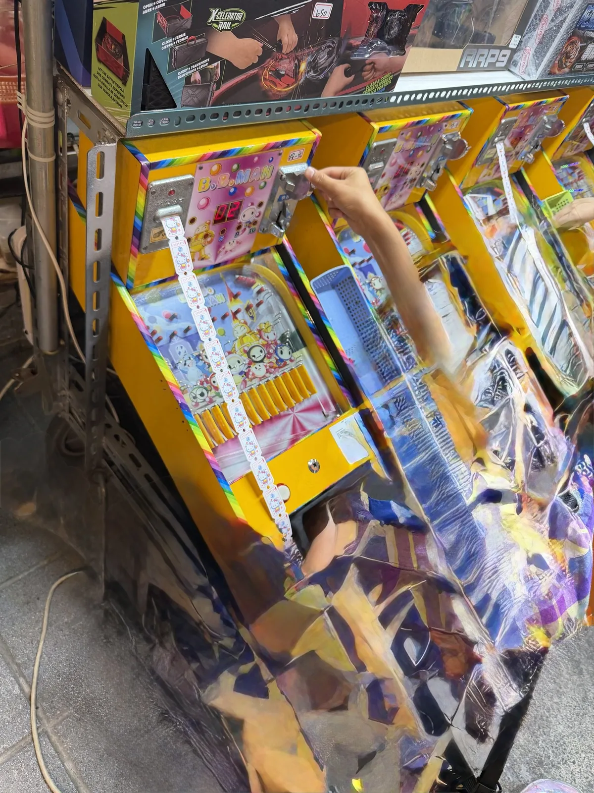 夜市のゲーム屋台。明るく光る筐体がずらりと並び、その前で子どもが手を伸ばして遊んでいる