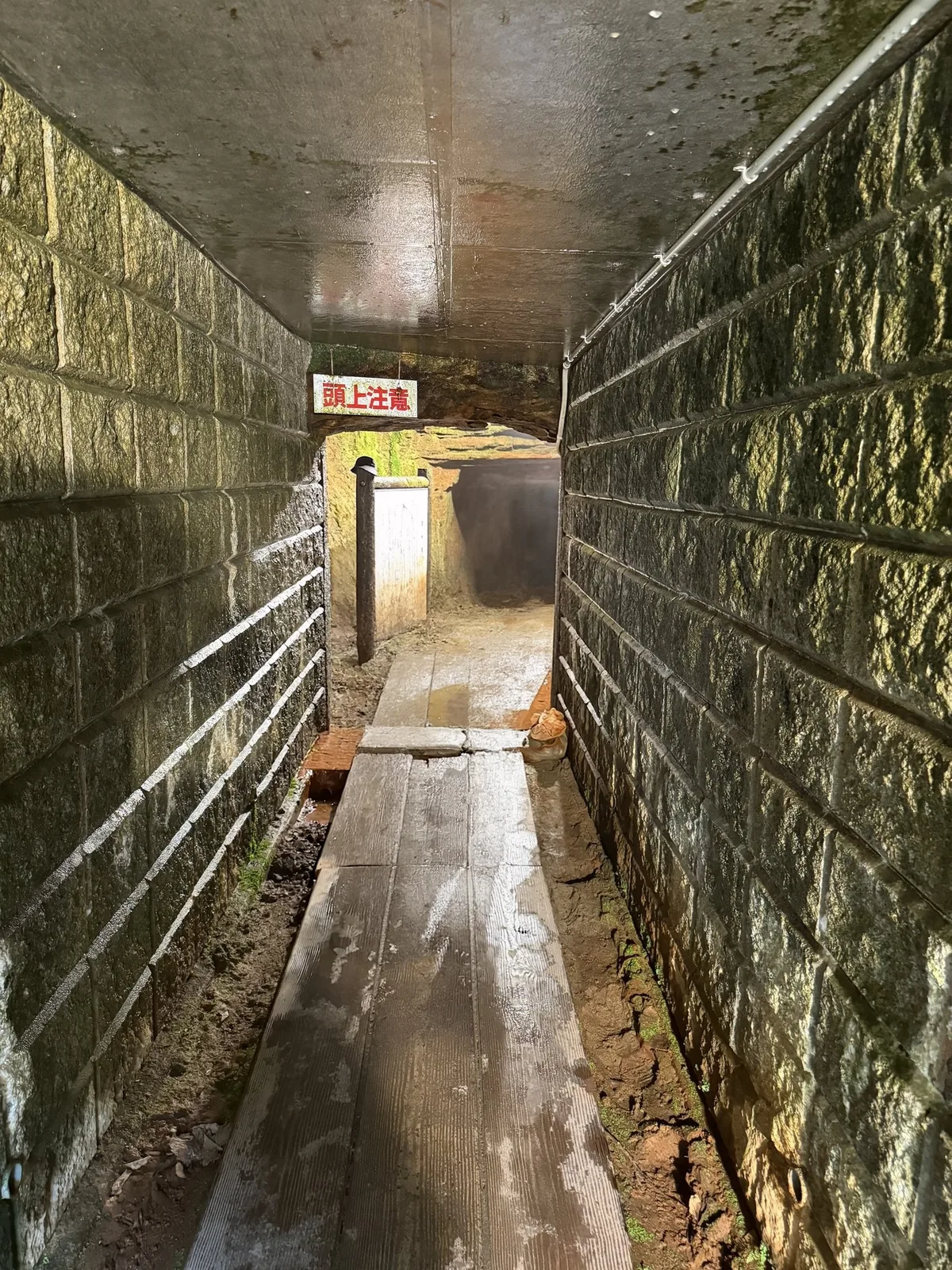 延沢銀山遺跡の坑道の中。狭い岩の通路に板の歩道が続き、奥に「頭上注意」の札がある