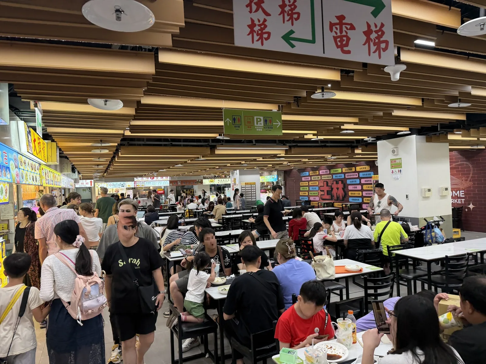 士林夜市B1美食區の内部。エスカレーターと電梯の案内が出た通路沿いに客席が広がっている