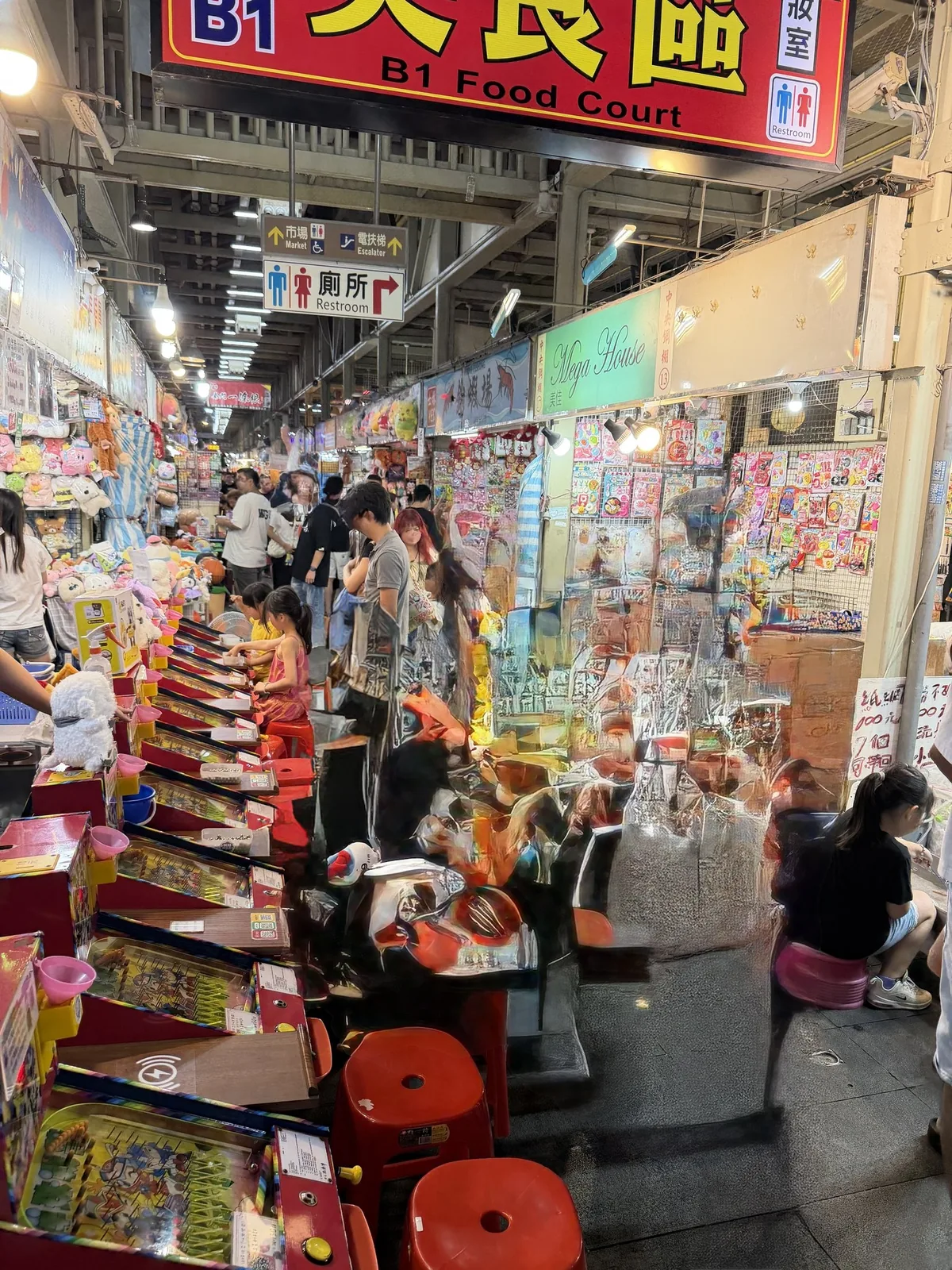 士林夜市B1美食區の看板の下に並ぶゲーム機。赤い椅子が置かれ、客が座って遊んでいる