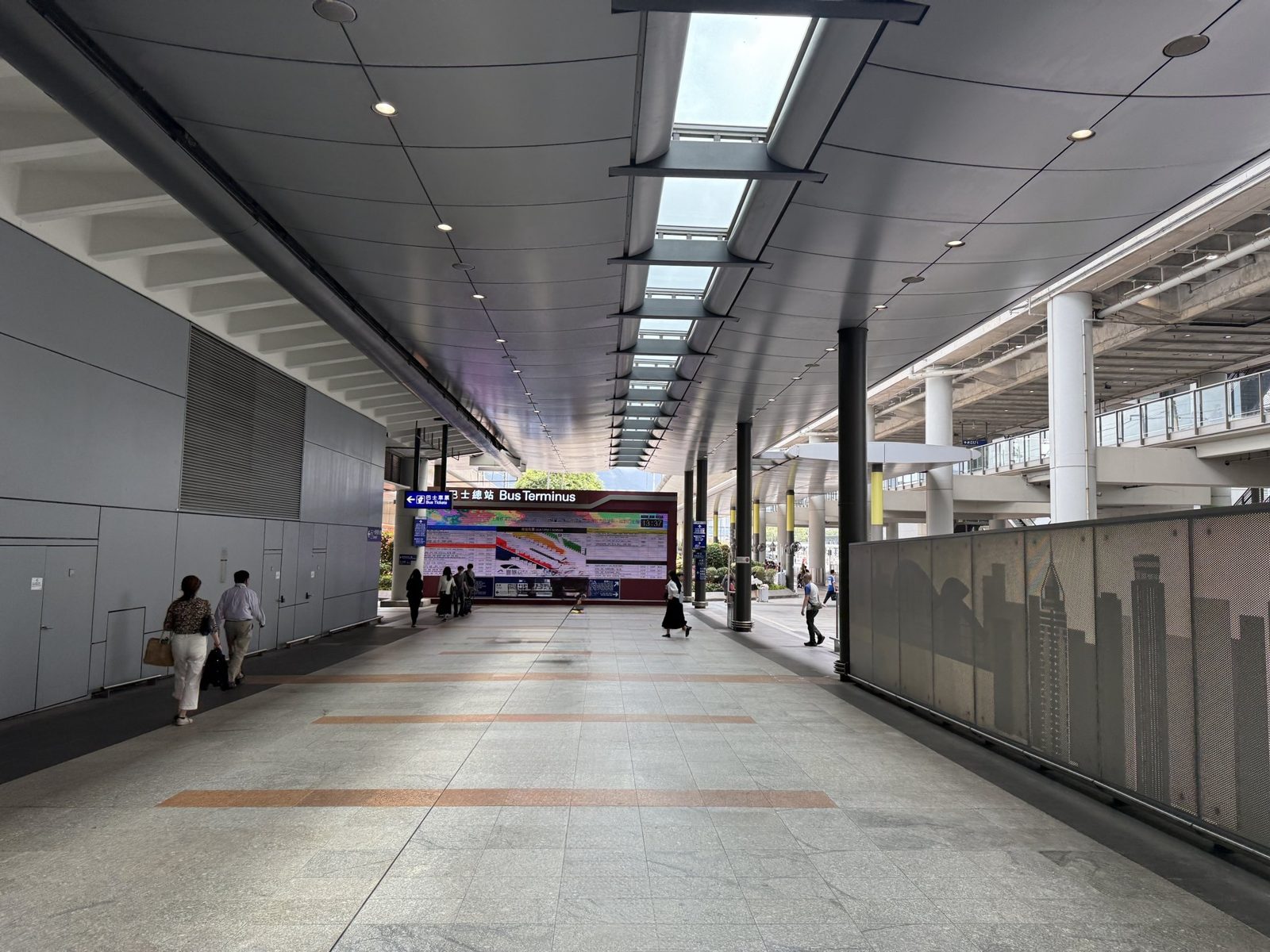 荃灣西駅とホテルをつなぐ屋根付きの歩行者デッキ。段差がなく平坦で、奥にバスターミナルの案内板が見える