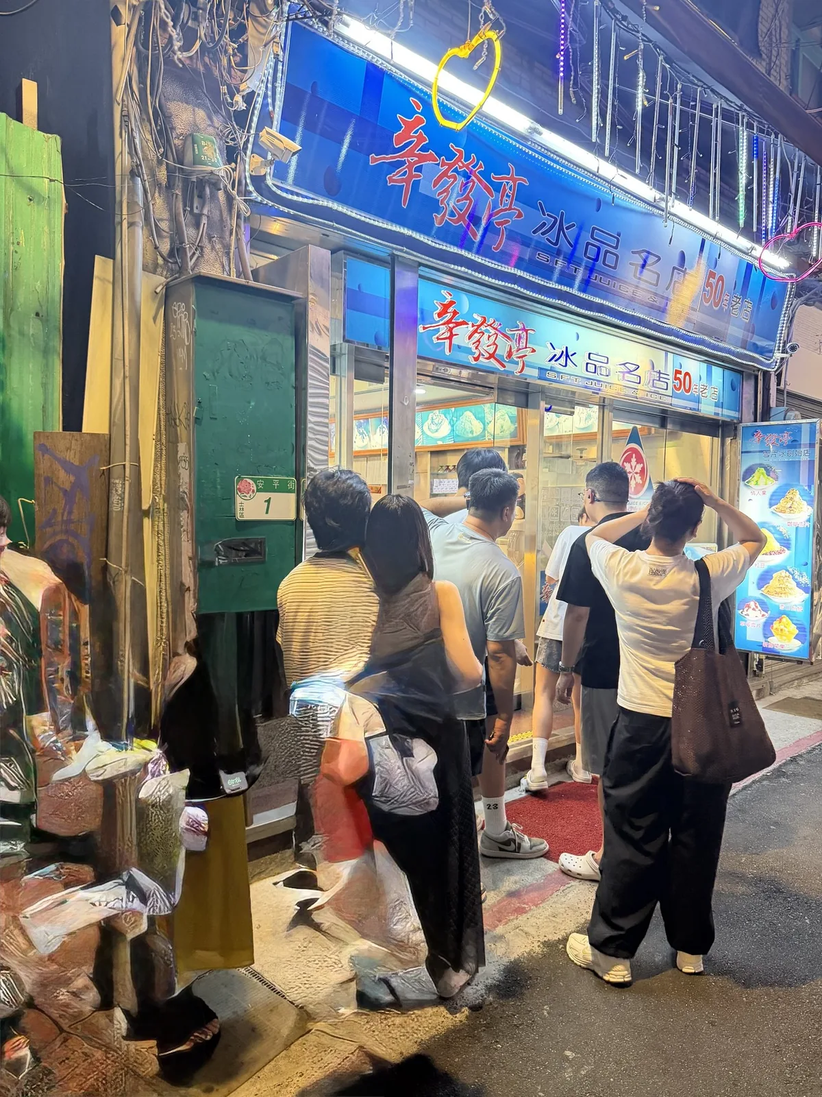 辛發亭の店先。青いネオンの看板が明るく光り、夜の通りに客が列をつくって並んでいる