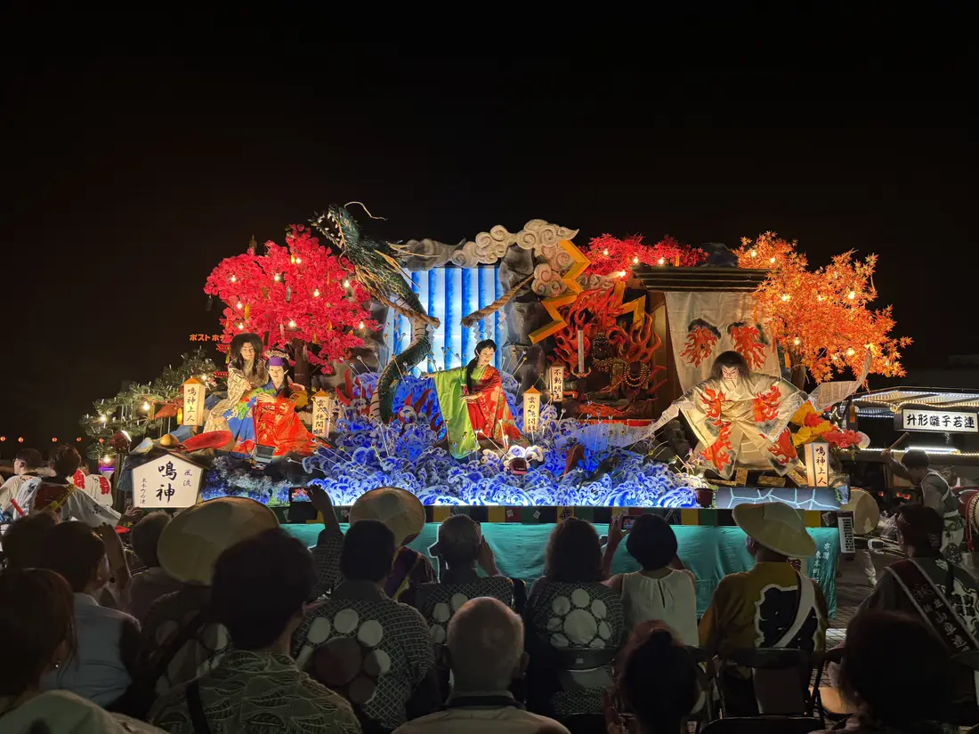 新庄まつりの宵祭。色とりどりに照らされた山車と、前に並ぶ観覧席の人たち