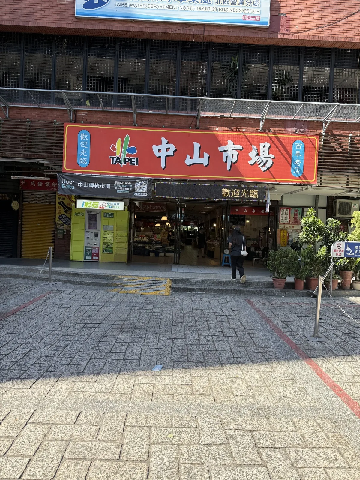 中山市場の入口。通りに面した看板の下に、買い物客がまばらに出入りしている昼の様子