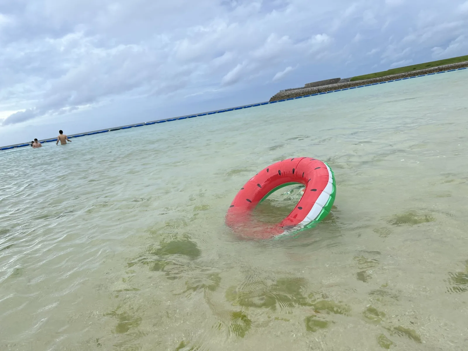 アラハビーチの浅い海に浮かぶスイカ柄の浮き輪。奥に防波堤とネットが見える