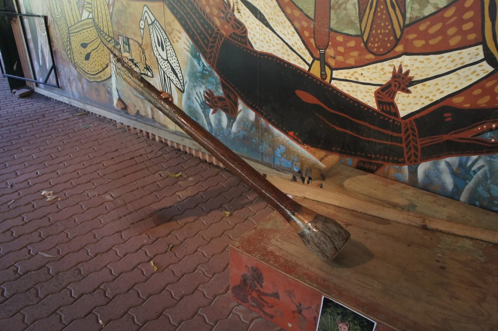 A large wooden club leaning on a wooden stand in front of an Aboriginal-art-style crocodile mural