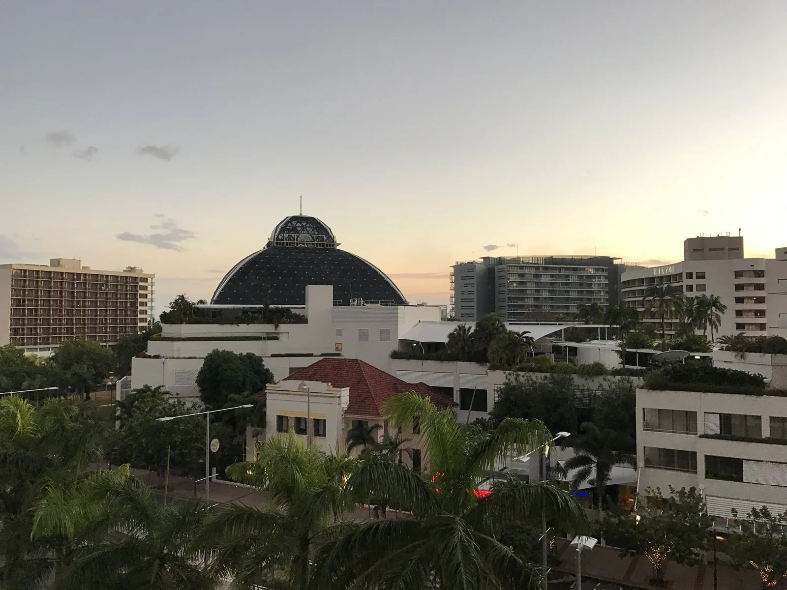 The Reef Casino’s glass dome and the Hilton building in the city at dusk, with palm trees in the foreground