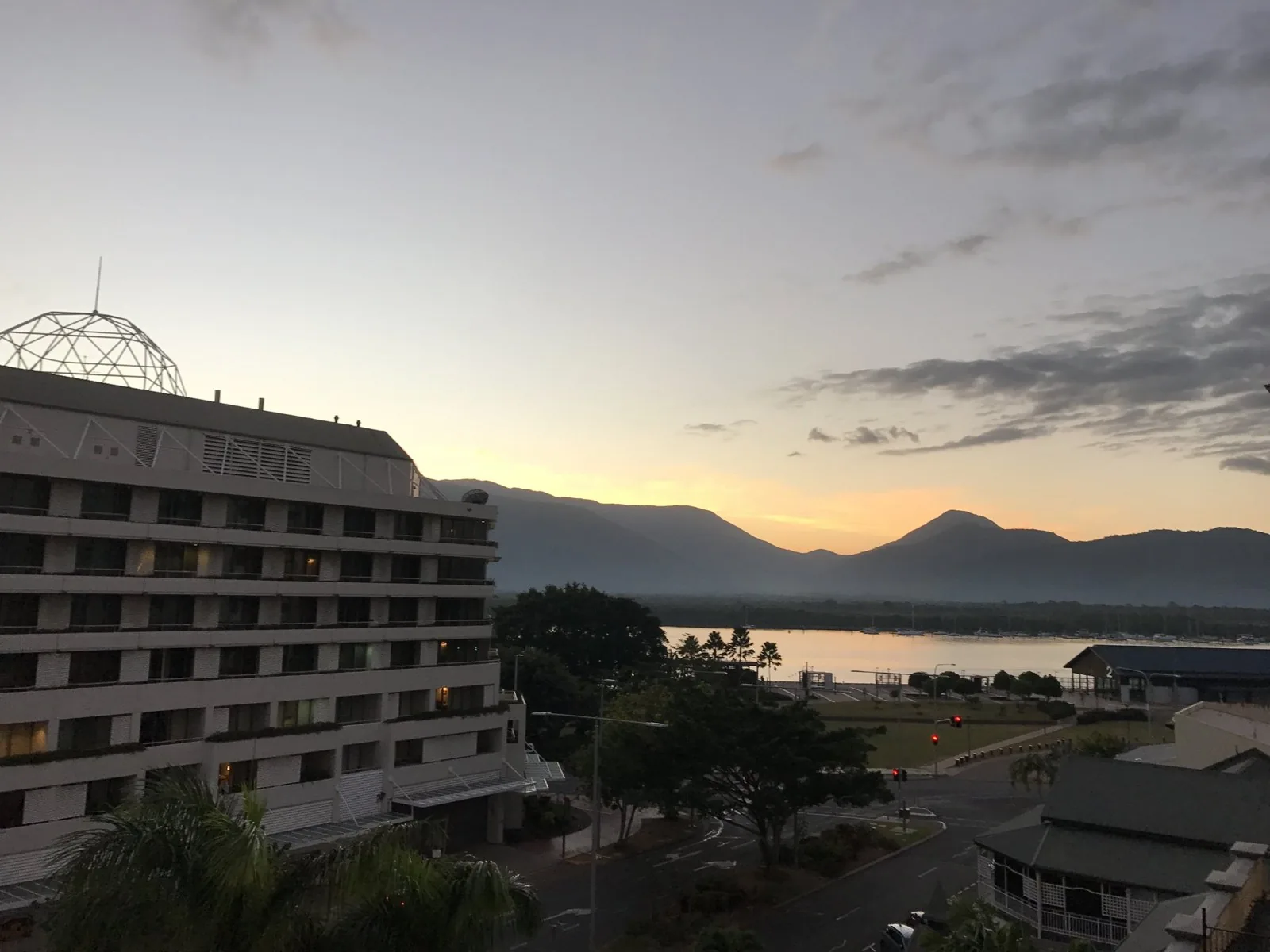 オレンジ色に染まる空の下、ドームのあるホテルと入江、奥に連なる山並みが見える街