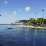 ケアンズ・エスプラネードのラグーンプールと日よけの屋根、魚のオブジェ、奥に広がる海