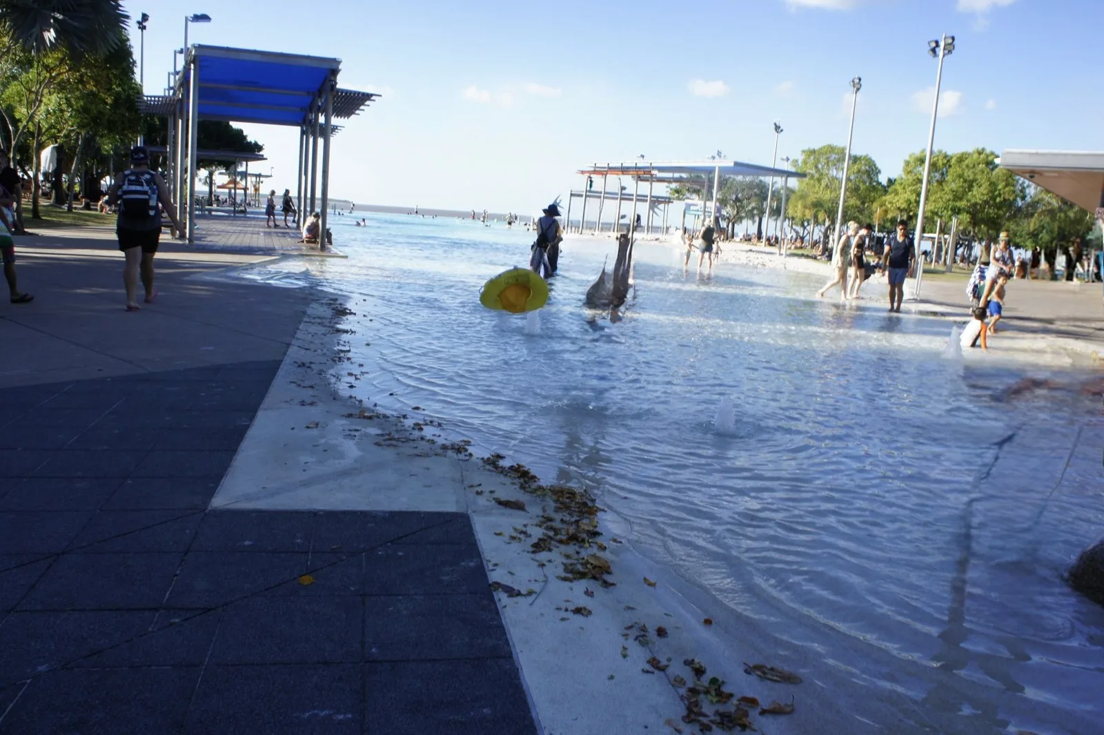ケアンズ・エスプラネードのラグーンプールで水に入る人々と青い日よけ屋根、奥に広がる海