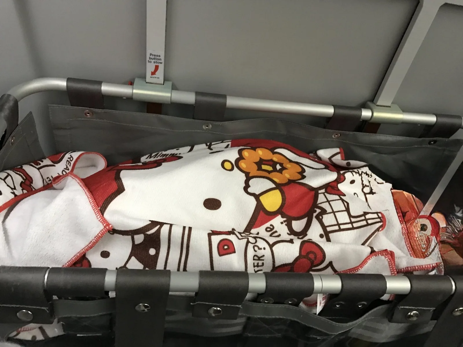 飛行機の壁に取り付けられたバシネットと、中にかけられたハローキティ柄のタオル