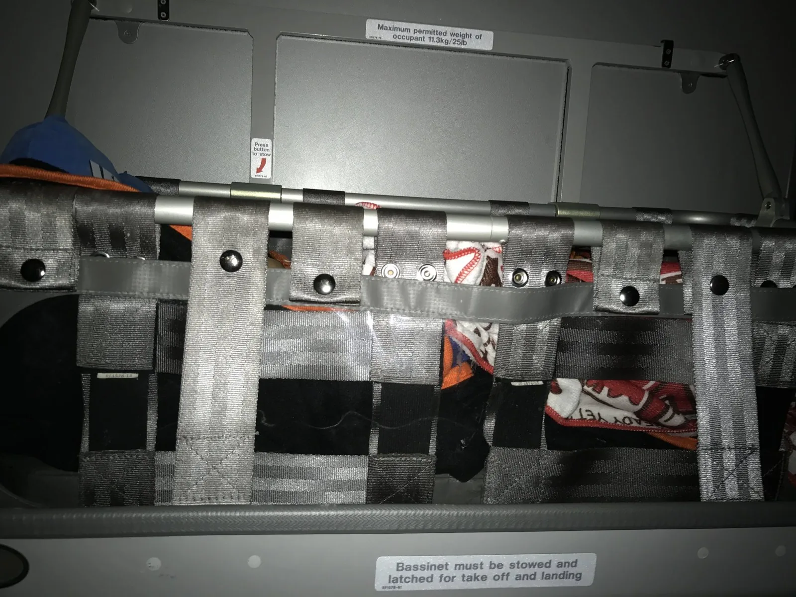 機内の壁に取り付けられた灰色のベルト枠のバシネットと体重制限11.3kgの注意書きラベル