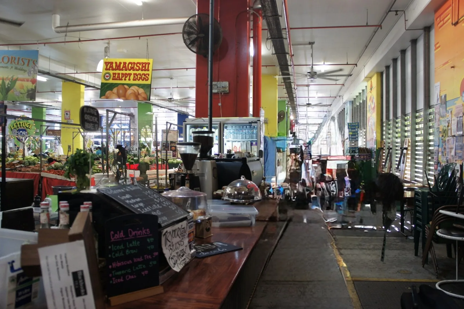 Chalkboard menus at a café counter in an indoor market, with an egg sign and produce stalls behind