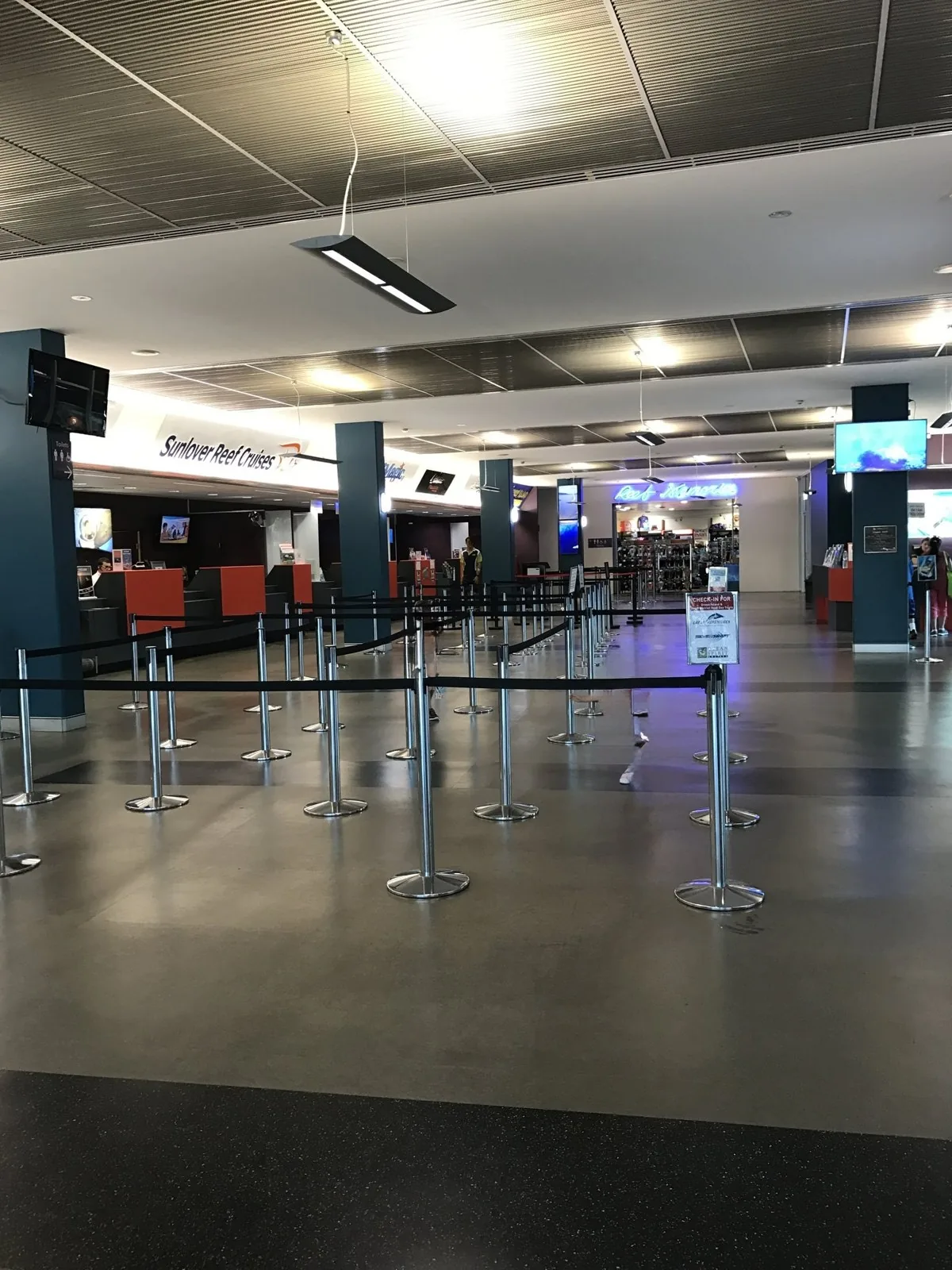 A check-in sign for Green Island and a roped-off waiting line, with cruise company check-in counters lined up in the back