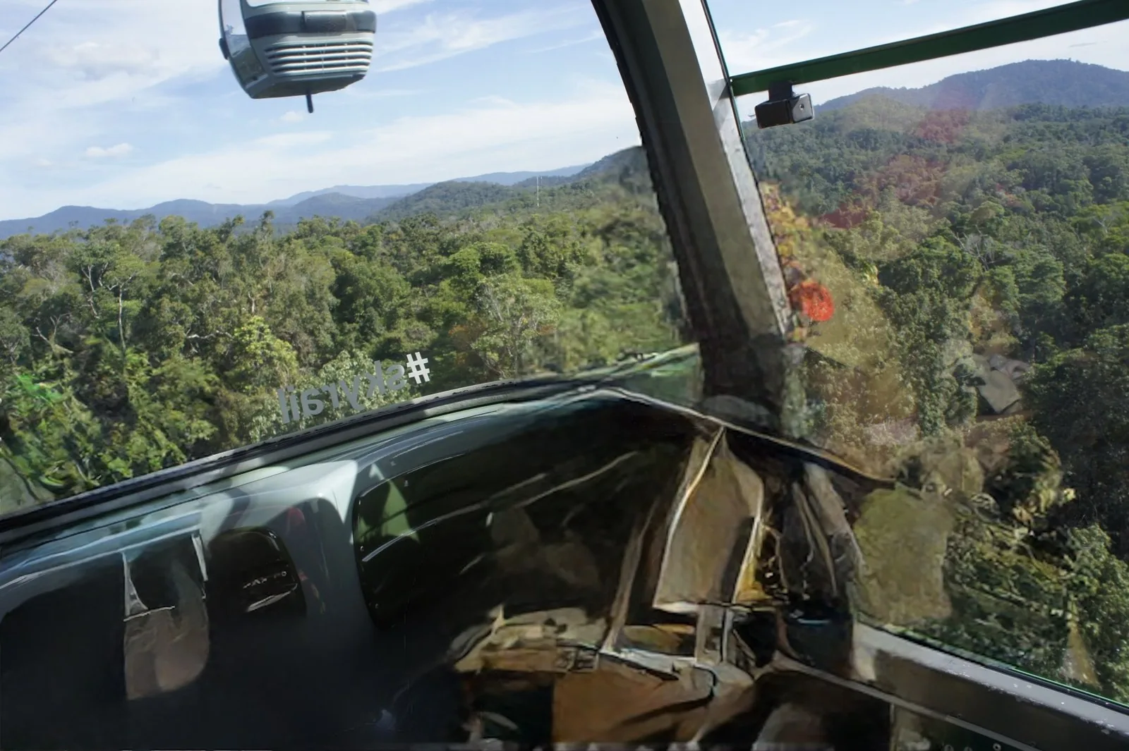 The gondola ahead and rainforest-covered mountains seen from the window of a Skyrail gondola