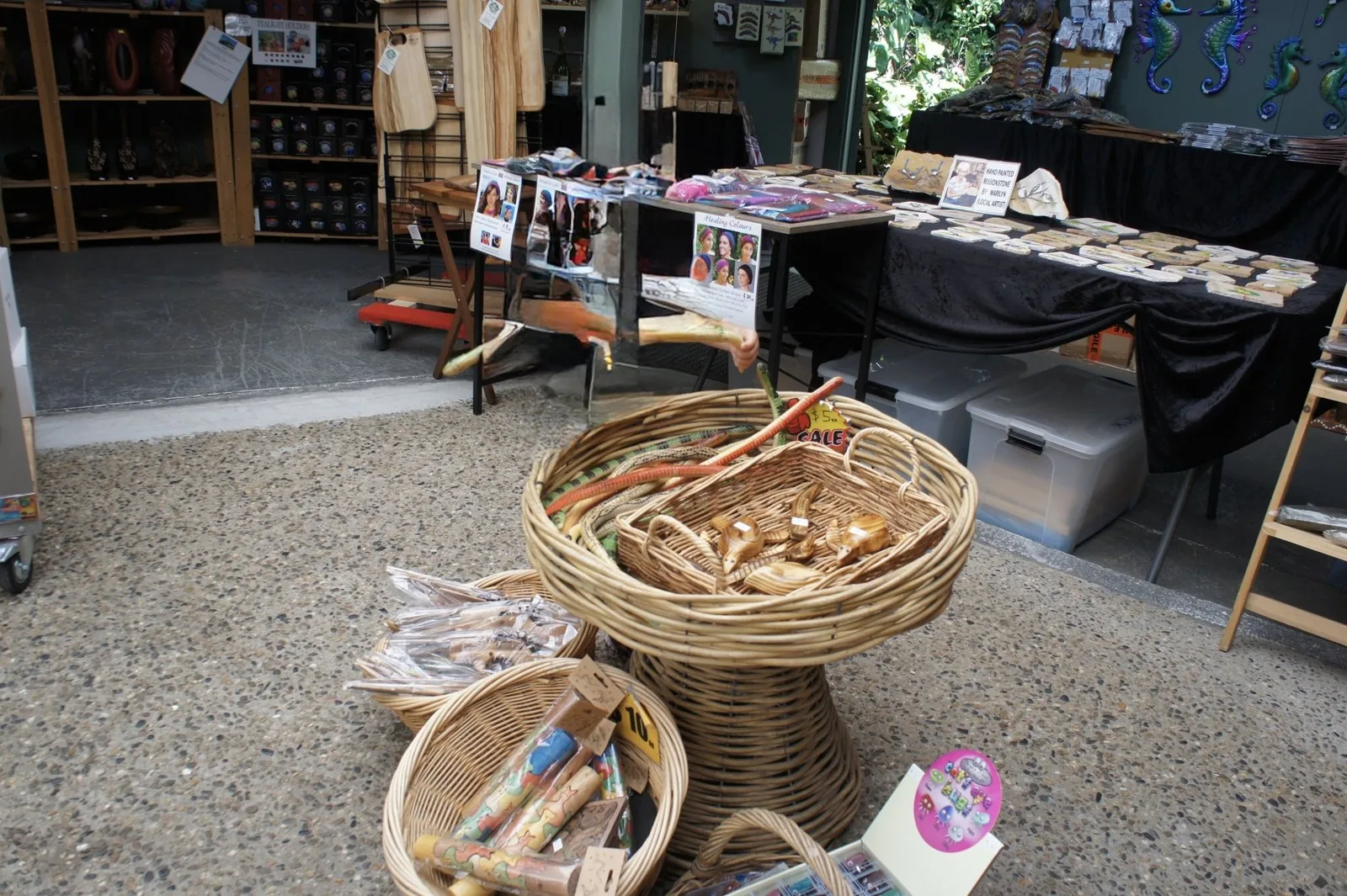 Wooden snake and animal carvings in rattan baskets on the floor of a souvenir shop, with hand-painted stone ornaments lined up behind