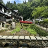 夏の銀山温泉。銀山川に沿って木造の旅館が並び、奥に赤い欄干の橋、手前に石の橋が見える