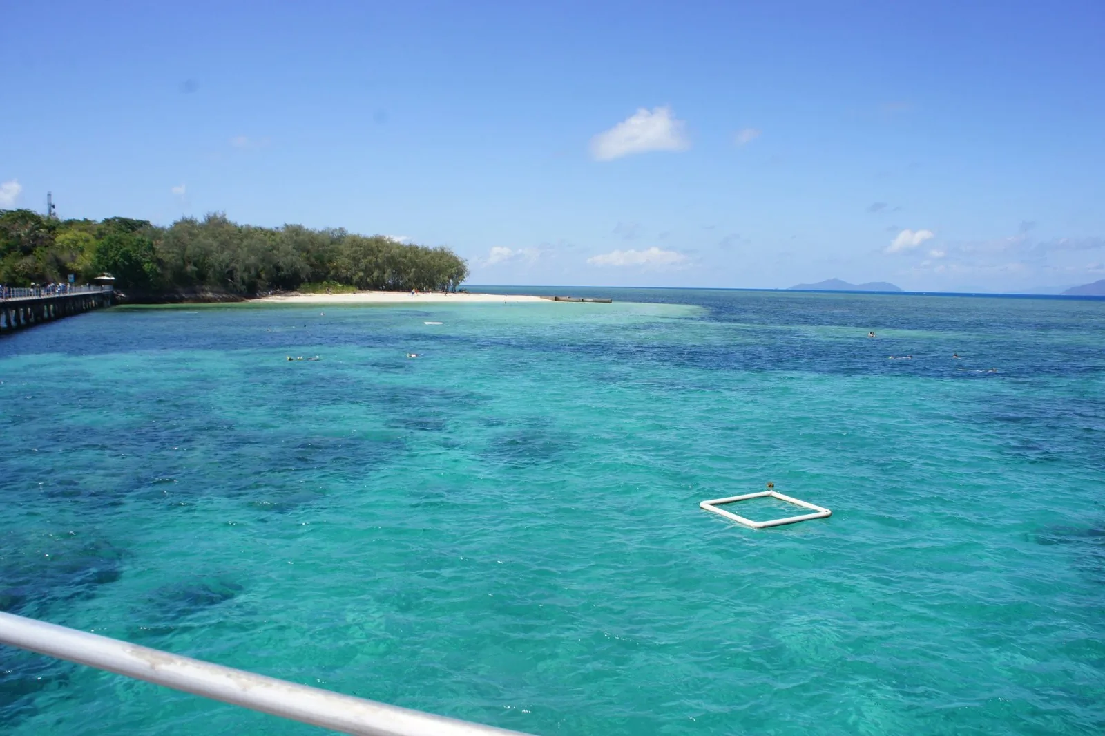 桟橋から見たエメラルドグリーンのサンゴ礁の海と、木々に覆われた島の白い砂浜