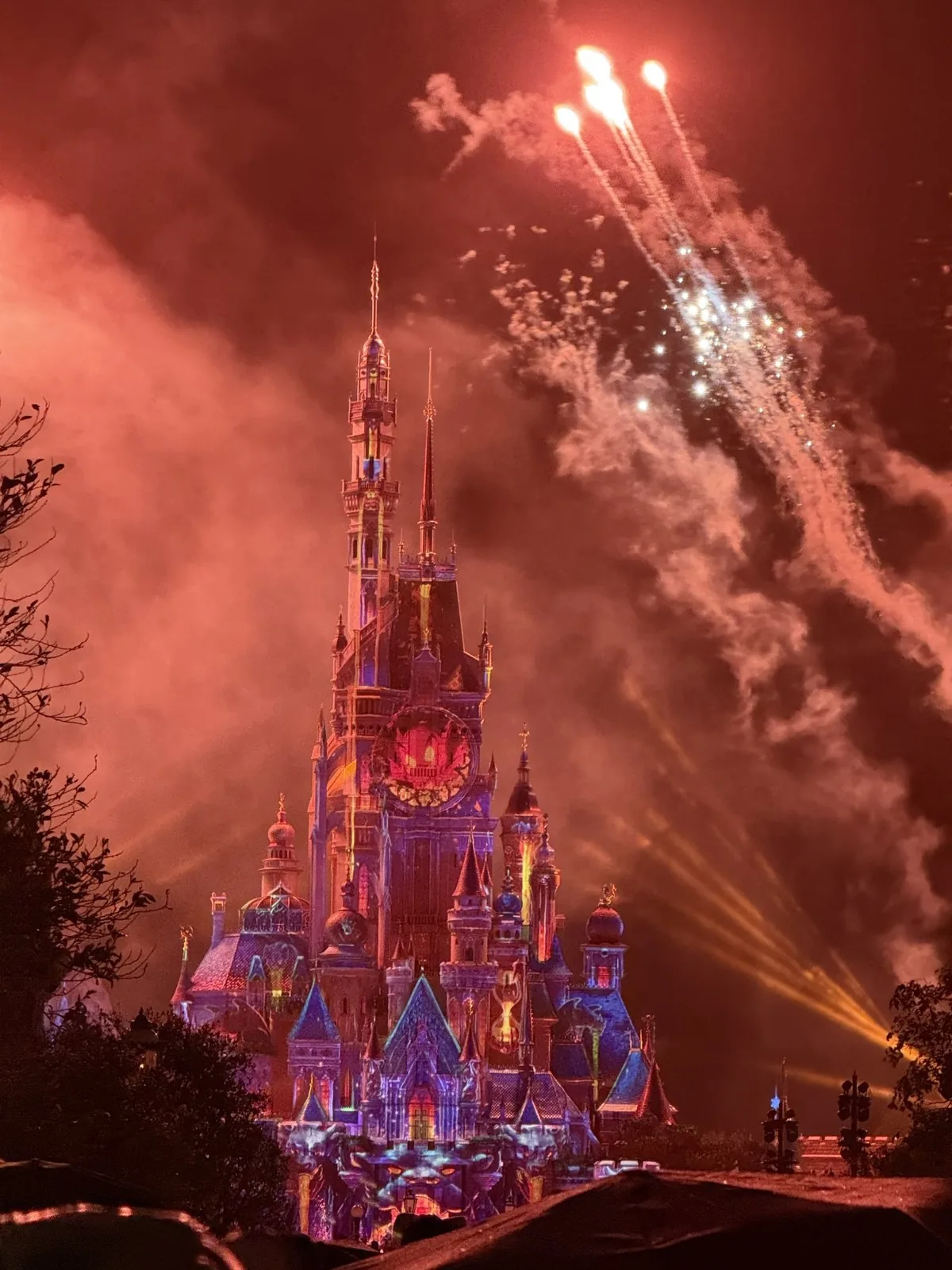 香港ディズニーランドの城に映るプロジェクションマッピングと、夜空に広がる花火と赤い煙