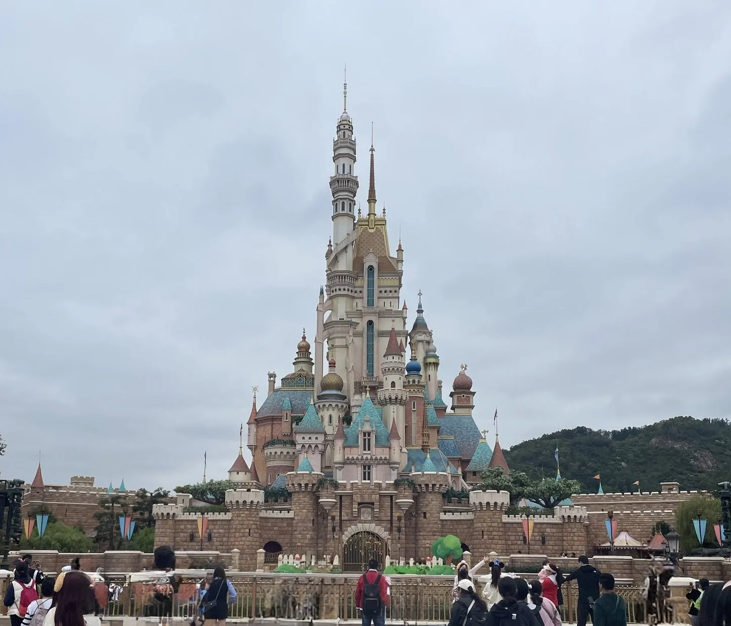 曇り空の下にそびえる香港ディズニーランドの城と、柵の前で城を眺める来園者たち