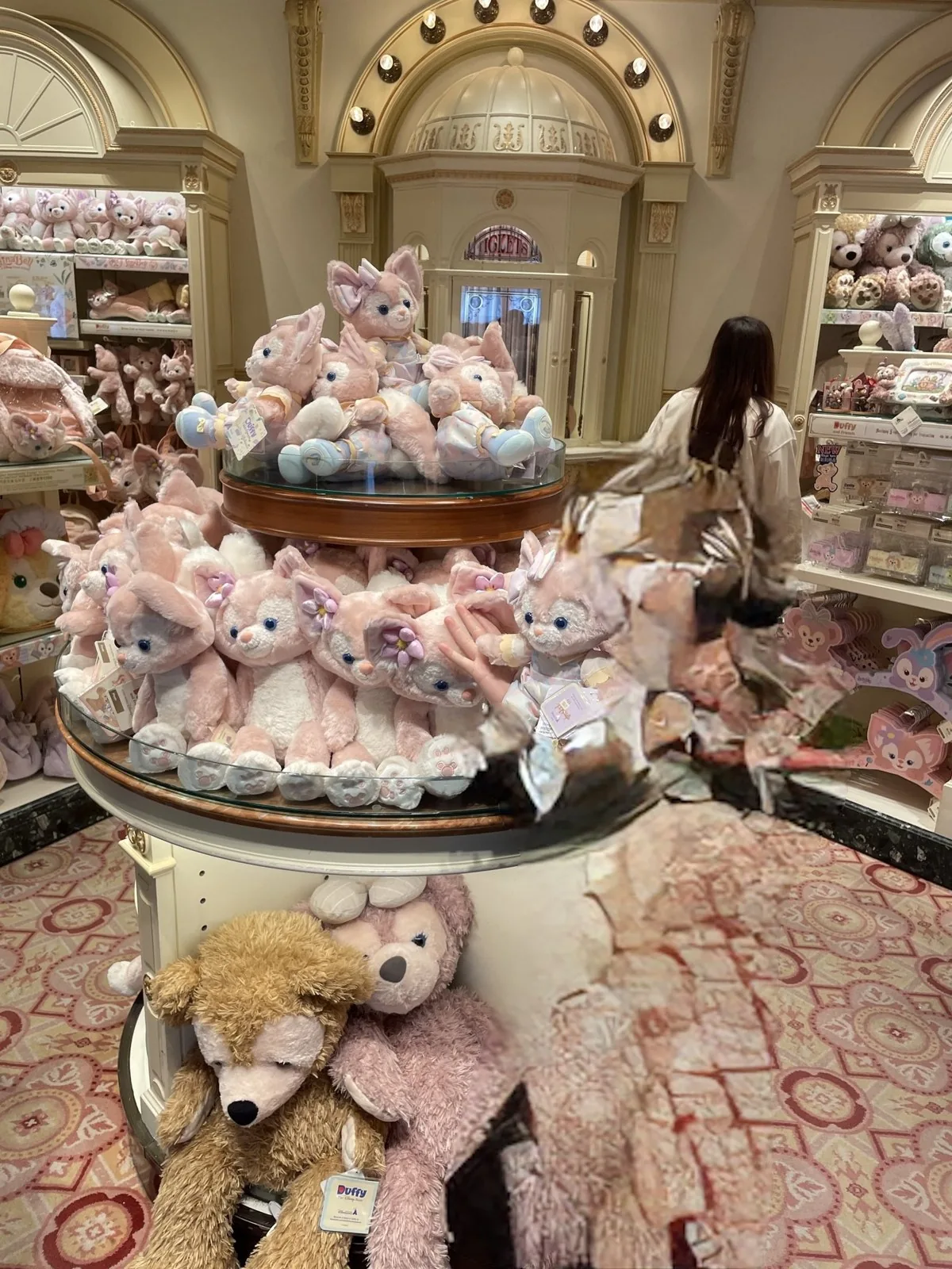 ショップの円形の陳列台に積まれたピンクのリーナ・ベルのぬいぐるみと、下段のダッフィーとシェリーメイ