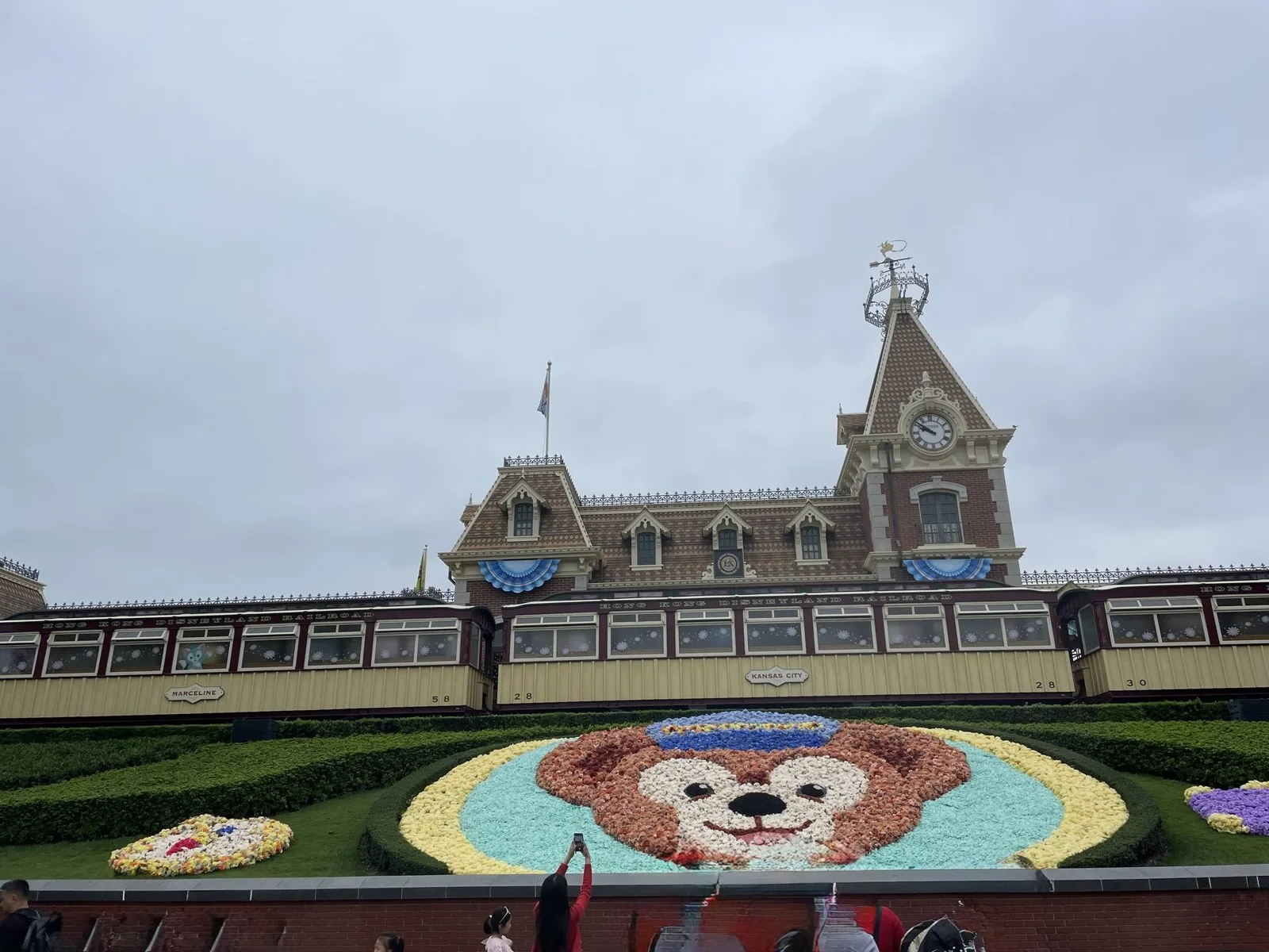 香港ディズニーランド鉄道の列車と時計塔のある駅舎。手前には花で作ったダッフィーの顔の花壇がある