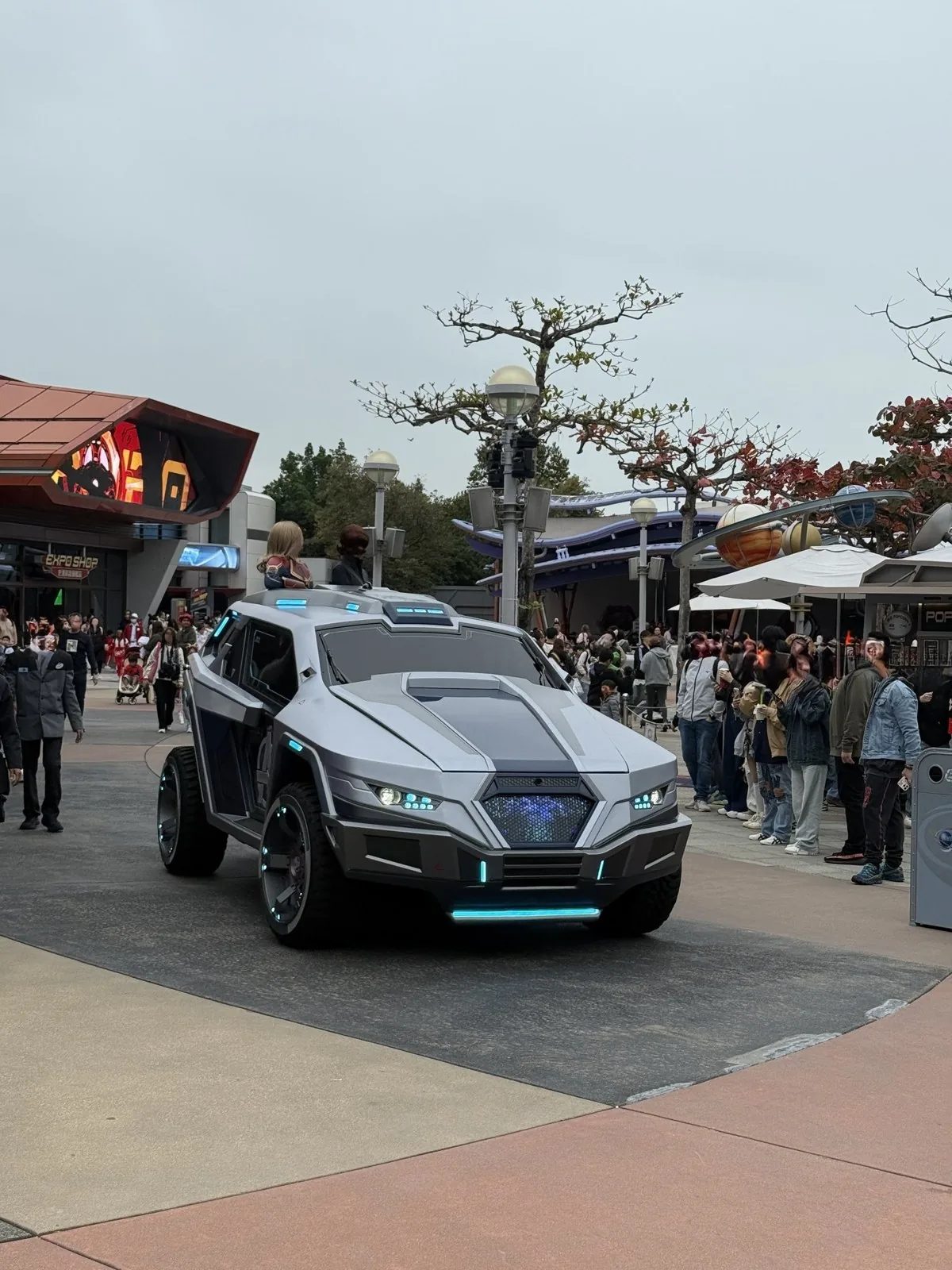 香港ディズニーランドのEXPO SHOPの前を走る銀色の未来的な車両と、その上に乗るキャラクター