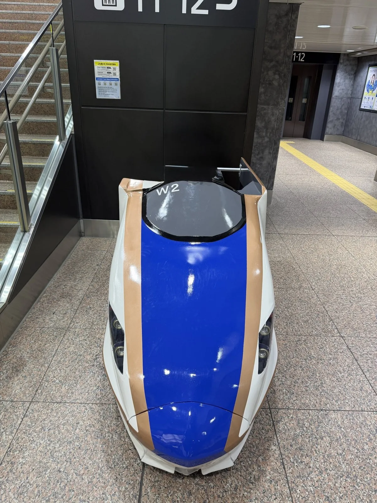 駅の11・12番線の階段前に置かれた、白と青と銅色の北陸新幹線W7系の先頭部のオブジェ