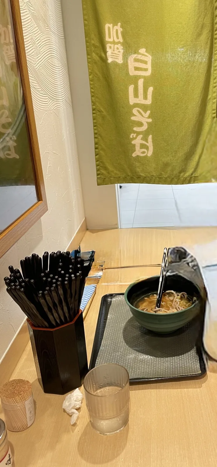 金沢駅の加賀白山そば。緑ののれんの前のカウンターに、そばのどんぶり