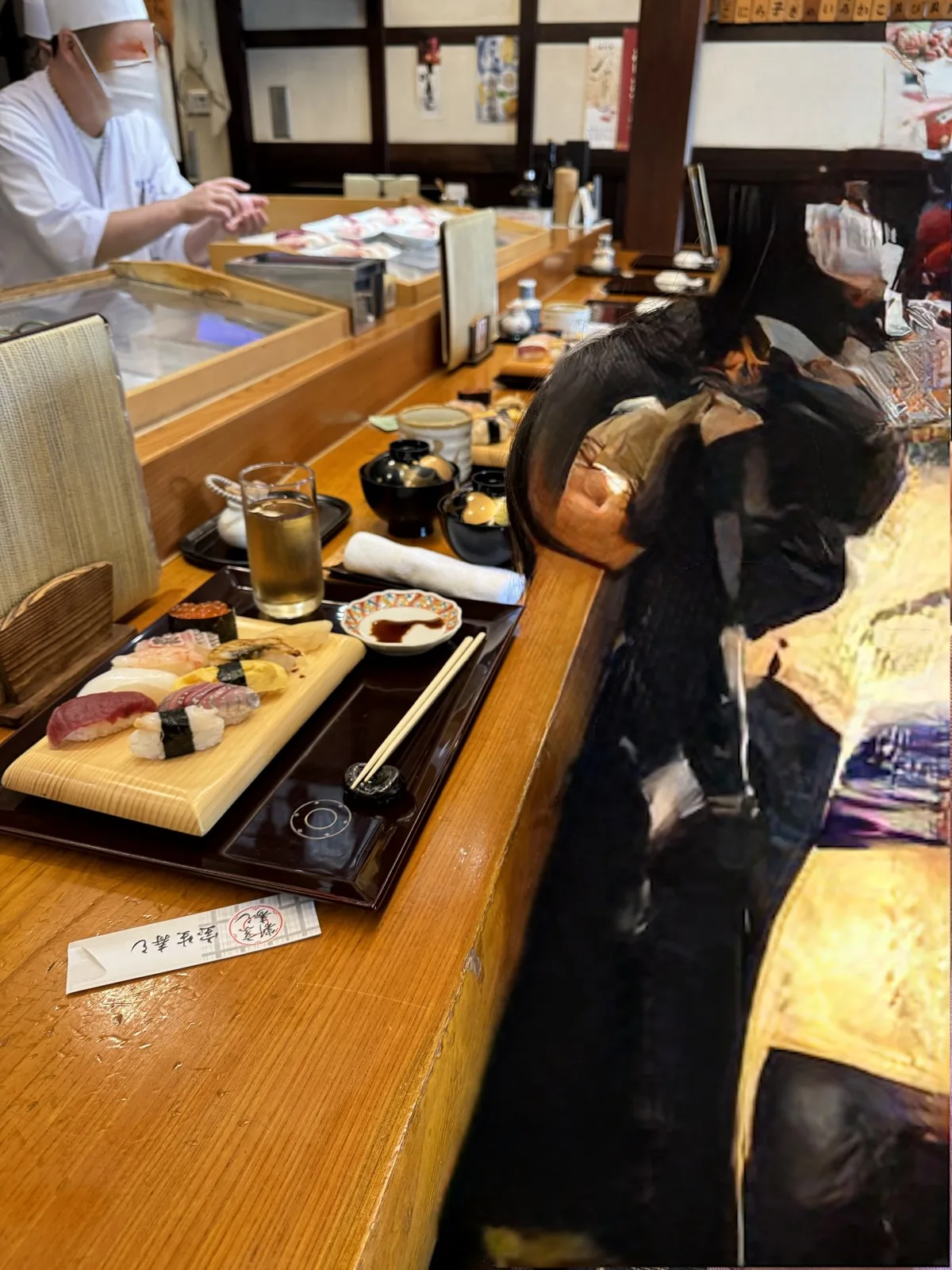 Assorted nigiri sushi lined up on a sushi restaurant counter, including tuna and salmon roe gunkan, with a soy sauce dish in front