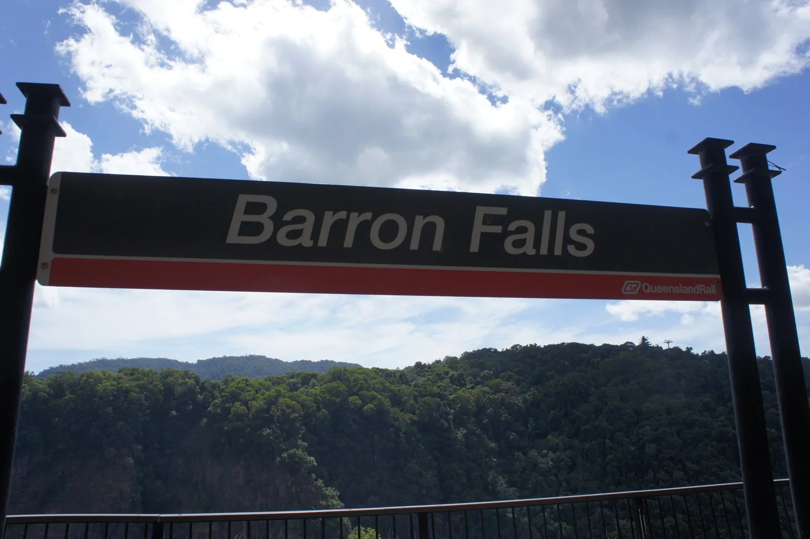 キュランダ鉄道バロン滝駅の駅名標と、その奥に広がる熱帯雨林の山並みと青空